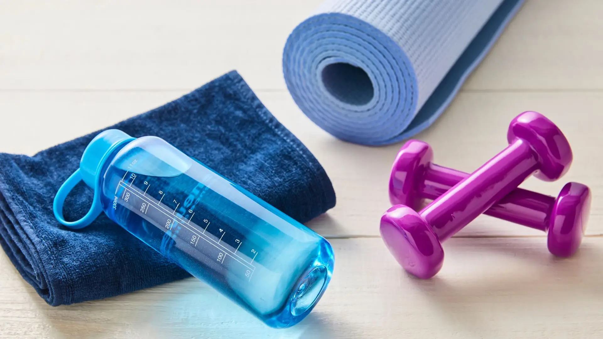 A shaker bottle, folded towel, yoga mat and dumbbells laid out before a workout.