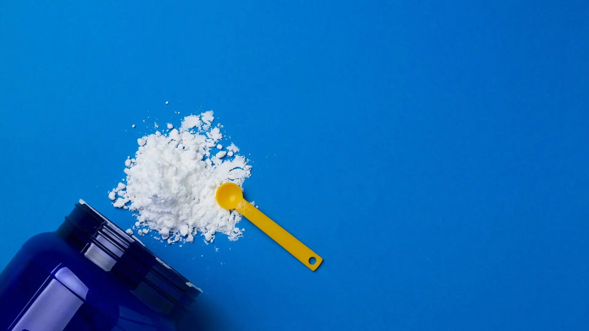 A scoop of white powder beside a drink bottle on a bright blue background.