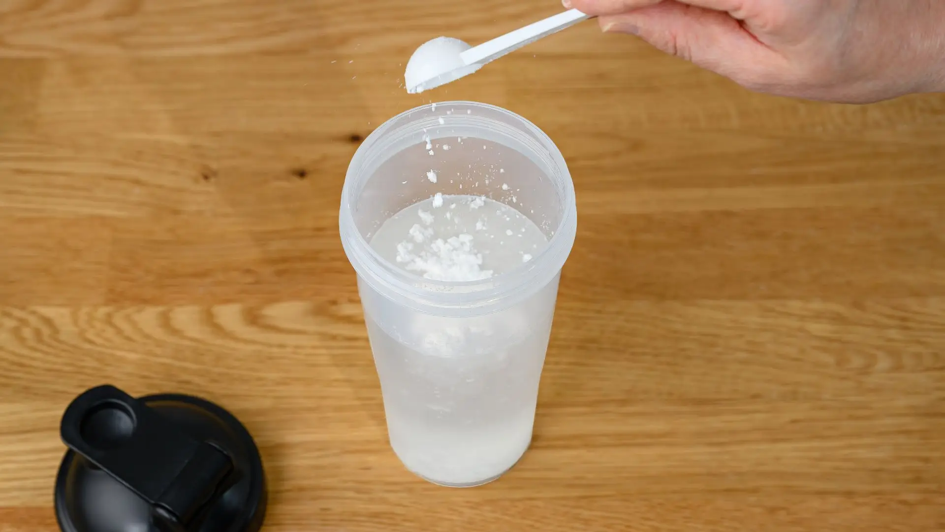 Powder being stirred into a clear glass of water on a wooden table.