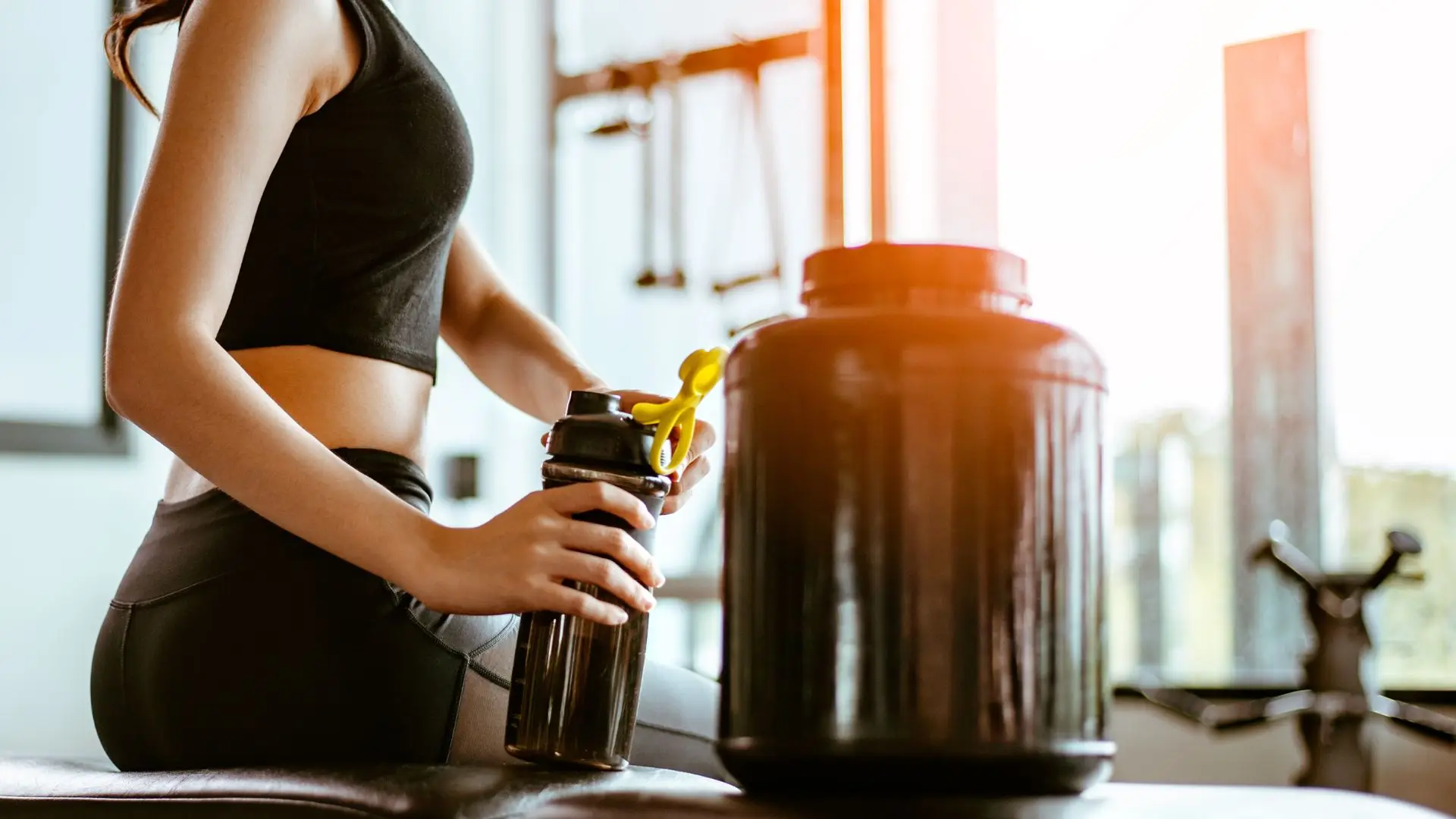 A woman in workout clothes holding a shaker bottle at the gym.